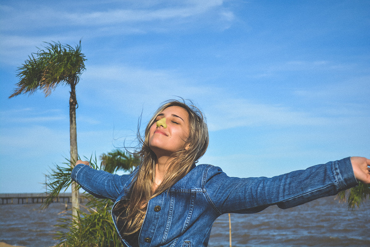 Woman enjoying the fresh air by the water while wearing her yellow Nöz stick nose sunscreen. 